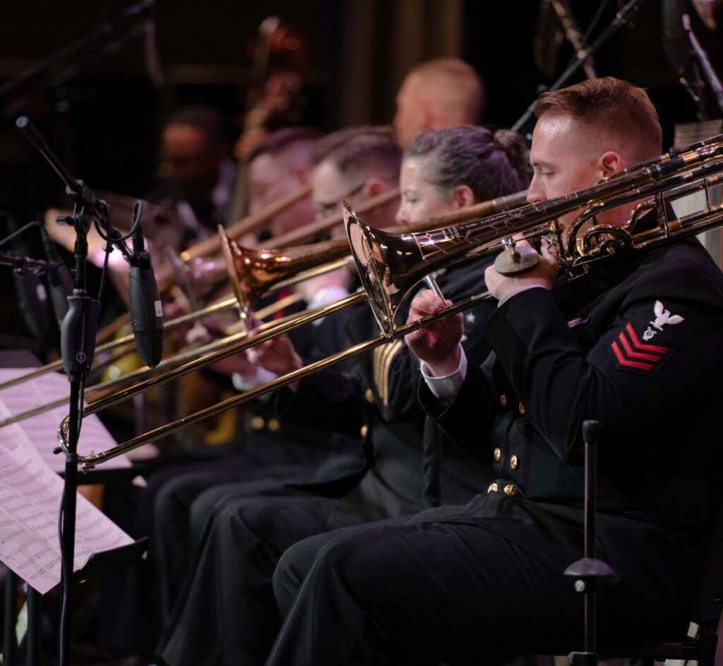 US Navy trombonist playing with other musicians in the background.