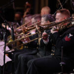 US Navy trombonist playing with other musicians in background.